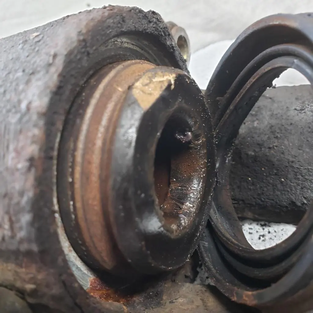 Damaged brake caliper piston with corrosion and a deteriorated protective dust boot